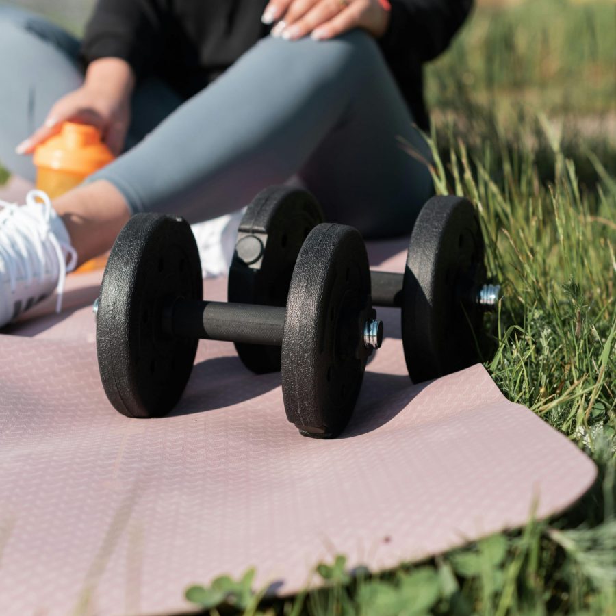 Woman exercising with dumbbells outdoors on a yoga mat.